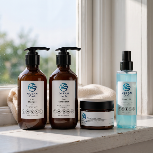Ocean Curls Full Routine Kit on a sunlit bathroom windowsill: two amber pump bottles of shampoo and conditioner, a black jar of leave-in curl cream, and a pale blue bottle of Ocean Mist sea salt spray